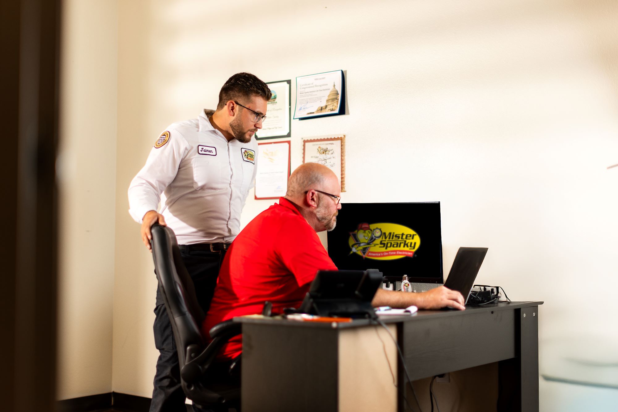 Mister Sparky franchise owner and technician looking at computer monitors with the Mister Sparky logo.