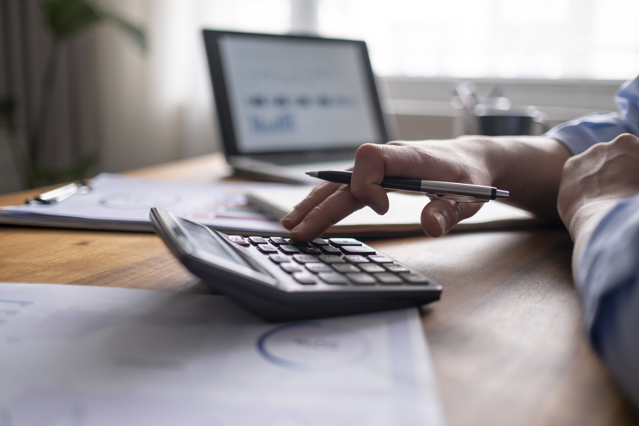 Business owner calculating startup costs with a calculator and laptop.